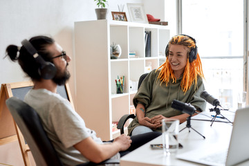 Two bloggers, young man and woman in headphones looking at each other while talking, recording...