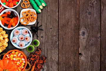 Fototapeta na wymiar Halloween candy side border over a rustic wood background with copy space. Variety of fun, spooky treats. Above view. Buffet party food concept.