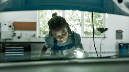 Getting your car on the road. Cropped shot of african american woman, professional female mechanic examining under hood of car with torch at auto repair shop
