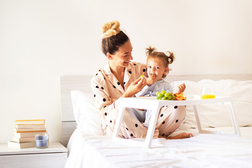 Mother and daughter having breakfast in bed with fruits in pyjamas - Family concept