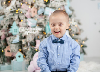 A little boy with Down syndrome at the New Year's tree, a child with a genetic disorder, children...