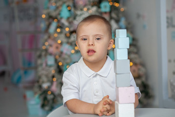 A little boy with Down syndrome builds a tower of blocks, a child with a genetic disease, disabled...