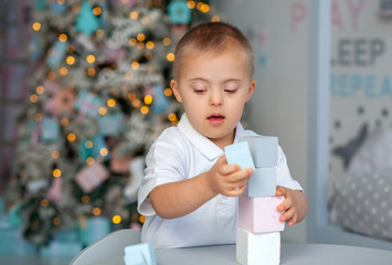 A little boy with Down syndrome builds a tower of blocks, a child with a genetic disease, disabled...