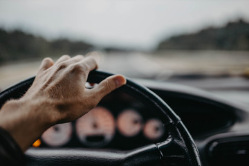 driving a car, hand on the steering wheel at sunset.