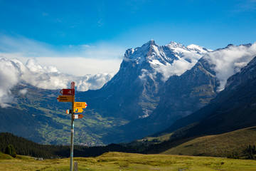 A trail sign at Klein Schendegg, Grindelwald and Wetterhorn mountain are in background.