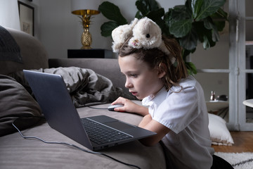 Little girl with the laptop on the sofa with school uniform on