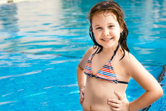 Smiling cute little girl in a swimming pool wearing bathing suit. Swimming course concept with empty copy space for Editor's content.