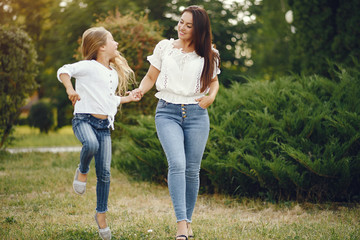 Fototapeta premium Family in a summer park. Mother in a blue pants. Little girl walking in a park.