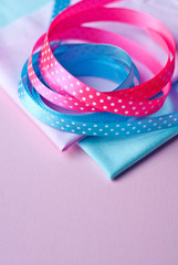 Cotton fabric of different colors and satin ribbons with polka dots on a pink background. Space for text, top view

