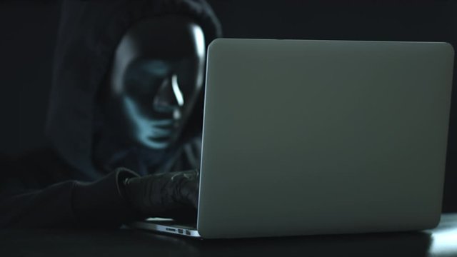 Unknown man wearing black mask steals information from a laptop. Hacking or darknet concepts