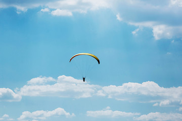 Yellow Paraglider flying into the sky with clouds on a sunny day