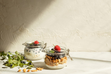 Healthy dessert with whipped cream, granola and fresh berries in a small jar. Light background, horizontal, with space