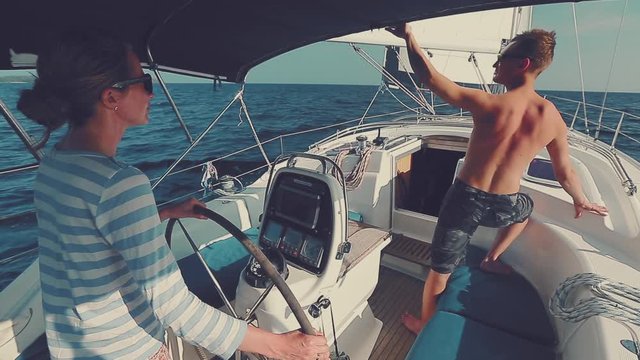 Couple sailing. Young couple sailing in the tropics, woman steers and man looks at the sails