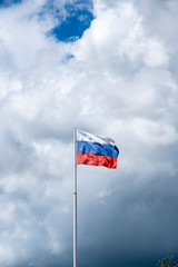 Russian tricolor flag waving in the wind against a cloudy sky.