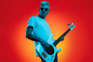 Stylish hipster man play white bass guitar in neon lights. Rock music concept.