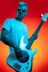 Trendy hipster man play white bass guitar in neon lights. Rock music concept.