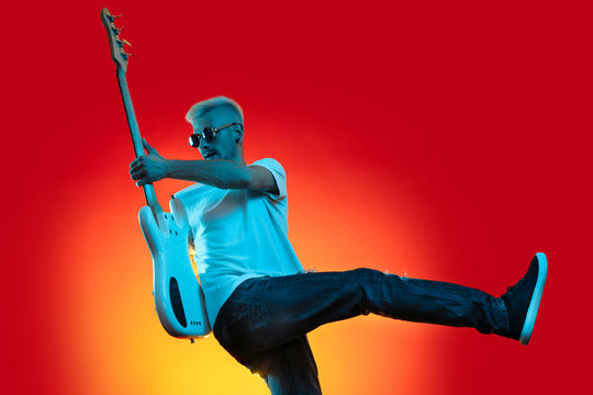 Talented blonde hipster man play white bass guitar in neon lights. Rock music concept.