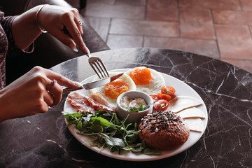 Girl having breakfast in cafe, eggs with bacon and fresh vegetables on black background.