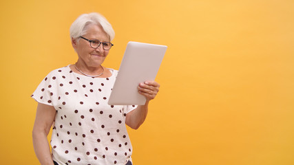 Senior woman having a video call on the tablet. Isolated on the orange background. High quality photo