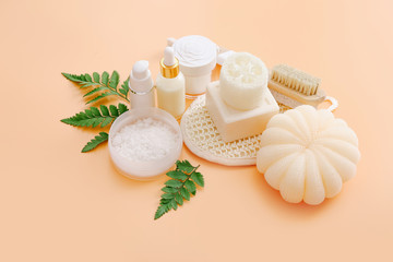 Bath accessories and natural cosmetics with green leaves on peach color background