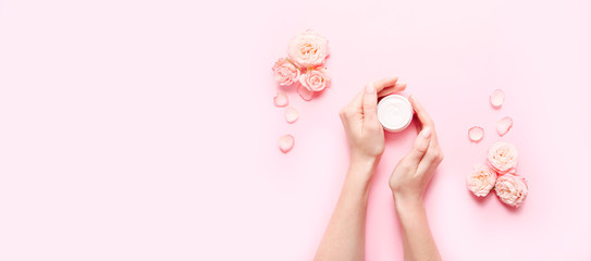 Skin care concept. Female hands with cream and roses flowers on pink background. Copy space