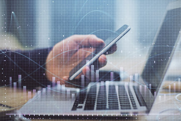 Double exposure of man's hands holding and using a phone and financial graph drawing. Analysis concept.