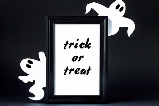 Background for Halloween. Black frame with the words "Trick or treat" on a black background. A white ghostly figure peeps out from behind the black lettering. Halloween typography concept and ideas.