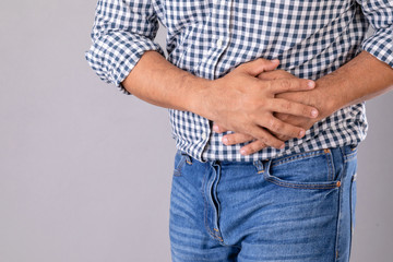 Stomach ache or pain on belly concept : Man using his hand and pressing on stomach on grey