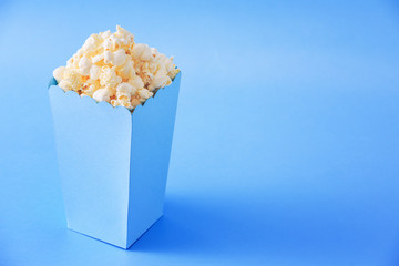 Blue bucket full of popcorn, isolated on blue background, with copy space next to it.