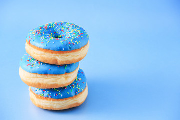 Stacked donuts with blue icing, isolated against blue background, with copy space next to hem.