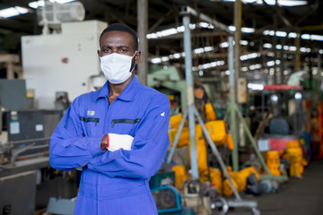Portrait of African American engineer worker wearing surgical mask with arms crossed in factory on a business day. New normal, epidemic prevention. Concept of Industrial manufacturing.