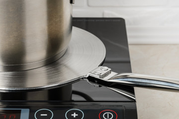Cookware on a stainless steel heat diffuser plate over a cooktop. Kitchen appliance for induction...