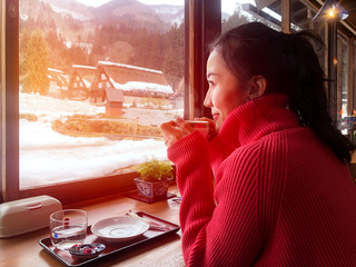 Woman tourist drinking coffee in the morning  and enjoying the winter snow view at Shirakawago village, Gifu, Japan.