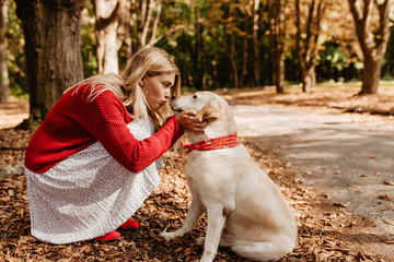 Beautiful woman kissing her adorable bonny dog. Lovely girl in red sweater and white dress sharing love with a pet.