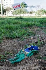 torn, dirty and rolled-up Brazilian flag thrown as garbage on dry foliage on land with a sale sign.