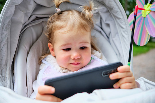 toddler sitting in baby carriage and playing game on her smartphone.