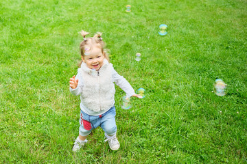Toddler chasing soap bubbles through a summer park.