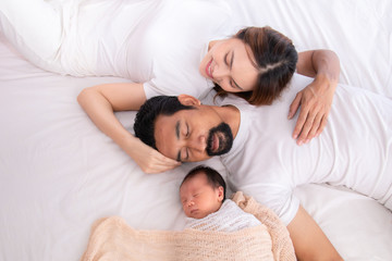 Obraz na płótnie Canvas Asian family lifestyle or mix race couple lying down on bed together relax comfortable, Asian Father with beard or Muslim dad and mother sleep hold/hug adorable newborn with love, care and protection