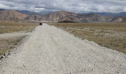 View of the mountains and dramatic sky and a car on the gravel road to Everest Base Camp, Tibet, China