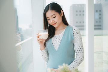 Young beautiful pregnant asian woman holding a cup of milk.