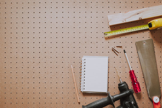 Top view of woodworking tools and notebook on pegboard background