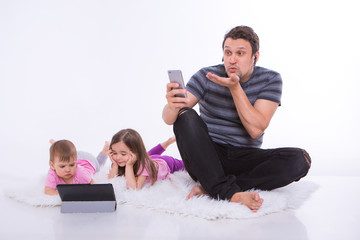 modern technologies in everyday life: a man talks on the phone through a headset, children watch a cartoon on a tablet. Hobbies and recreation with gadgets. Parent with girls on the floor