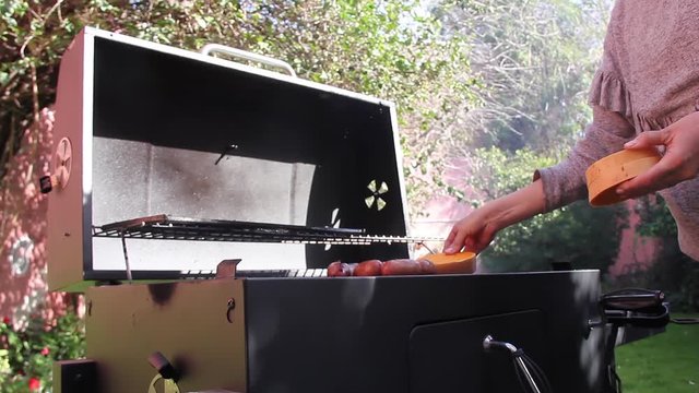 Pregnant Woman placing Pumpkins on Barbecue Grill with Pork Sausages.