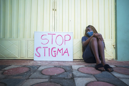 Young Black Female With A Medical Mask Sitting Next To A Sign With Text 