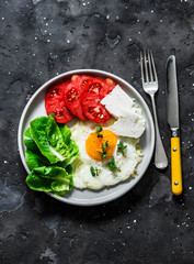 Delicious breakfast, snack, tapas - fried egg, ripe tomatoes, greek cheese, green salad on a dark background, top view