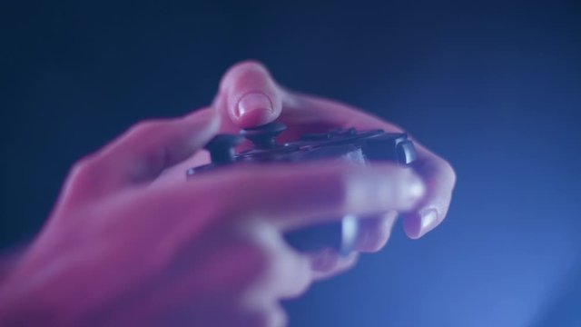 Playing video games on a small controller using joysticks playing quickly with blue lens flare black background