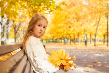 Naklejka na ściany i meble beautiful blonde teen girl sitting on a bench in an autumn Park with maple trees