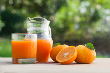 Orange juice on a wooden table and jug with tree and field background