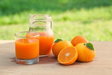 Orange juice on a wooden table and jug with tree and field background