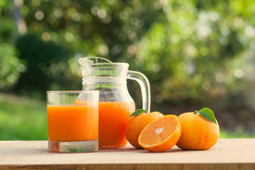 Orange juice on a wooden table and jug with tree and field background